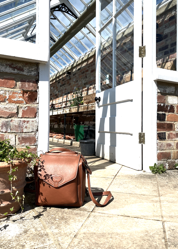 Brown leather bag on a stone floor with a glasshouse and brick wall in the background