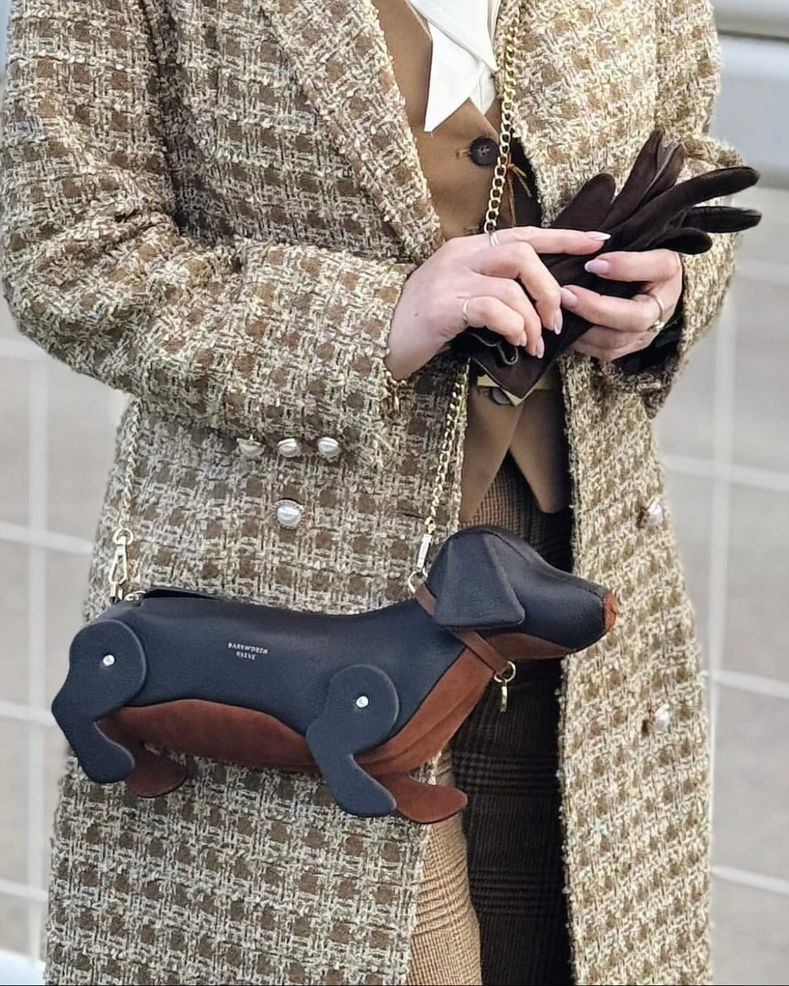 Person holding a dachshund-shaped handbag with a textured coat.