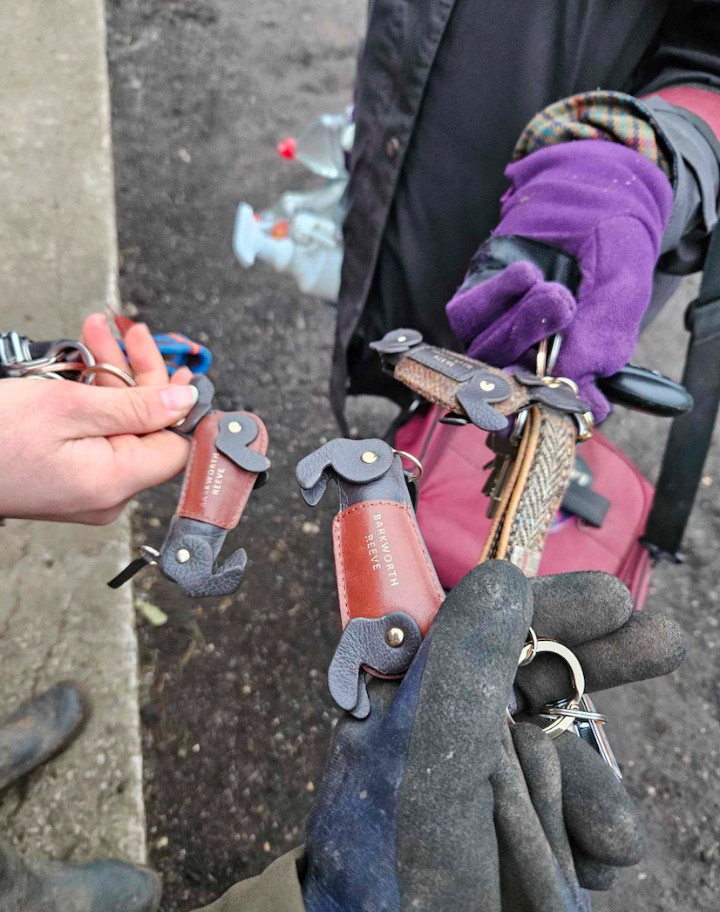 Person holding a keychain with multiple keys and tools, wearing gloves on an outdoor surface.