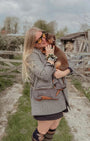 Woman holding a small dog outdoors with a wooden fence and trees in the background