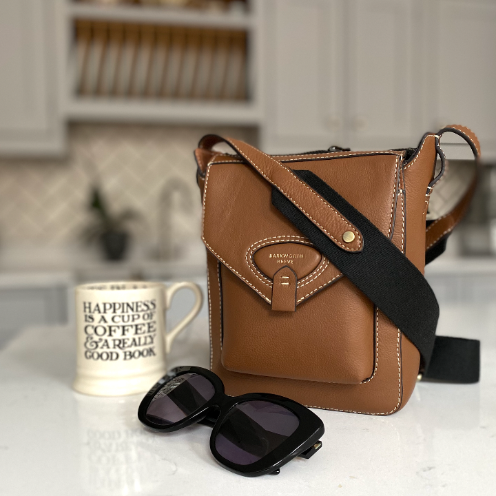 tan corss body bag on kitchen worktop with sunglasses and mug of tea