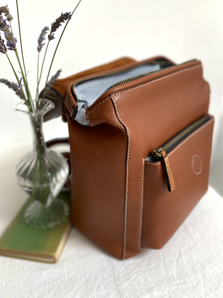 brown leather rucksack open with some flowers next to it 